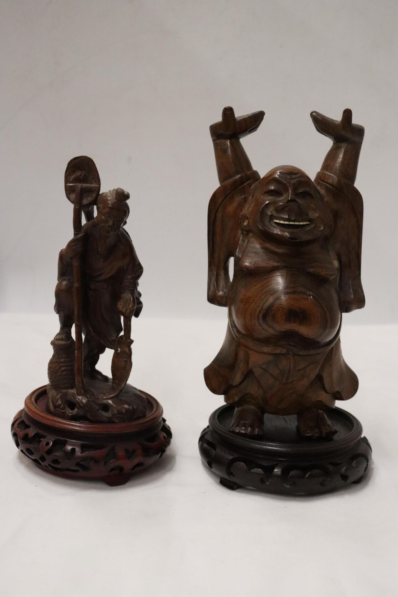 TWO CARVED WOODEN ORIENTAL FIGURES TO INCLUDE A LAUGHING BUDDAH, ON STANDS