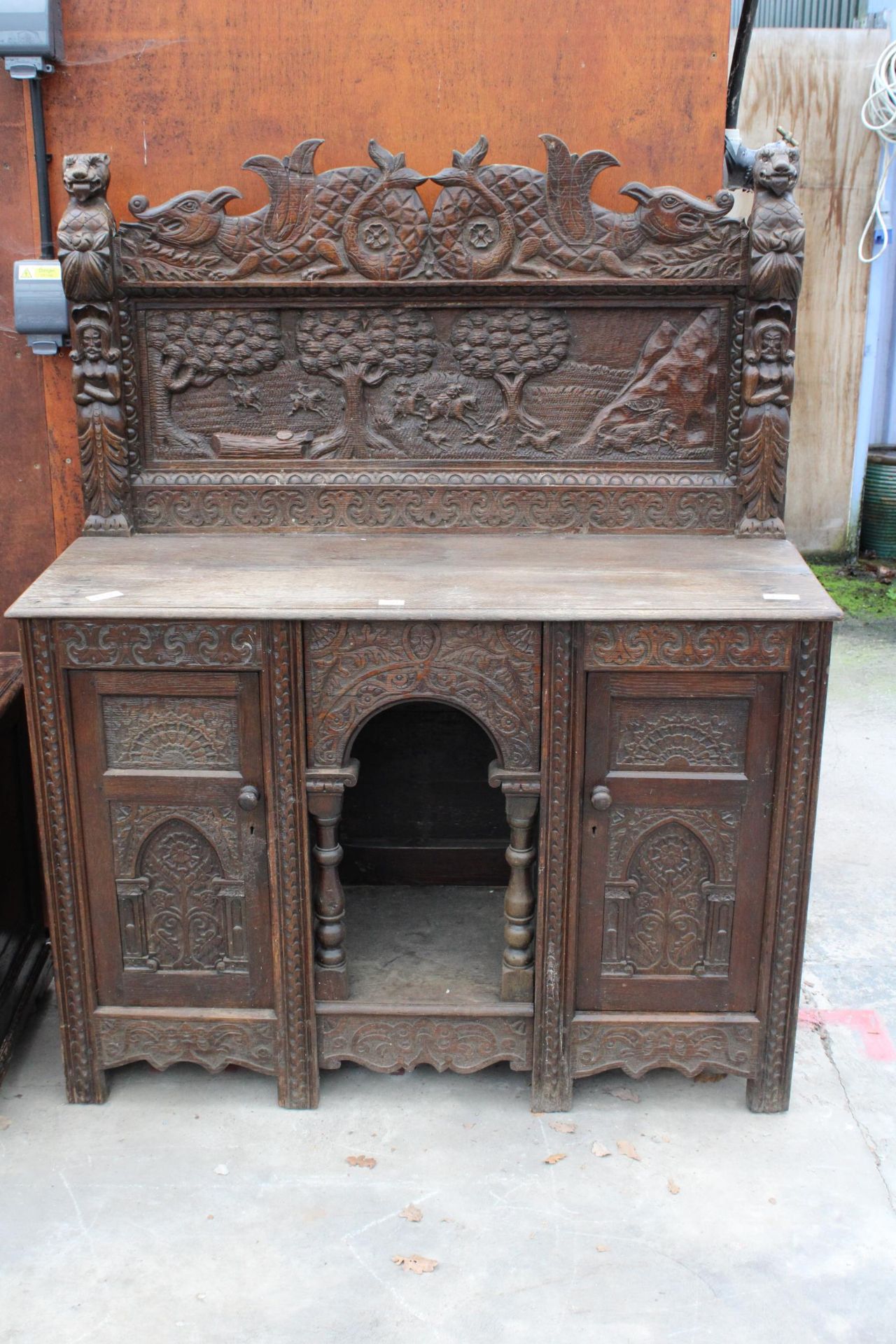 A HEAVILY CARVED GOTHIC OAK SIDEBOARD WITH DEER HUNTING SCENE AND MYTHICAL FIGURE, RAISED BACK,