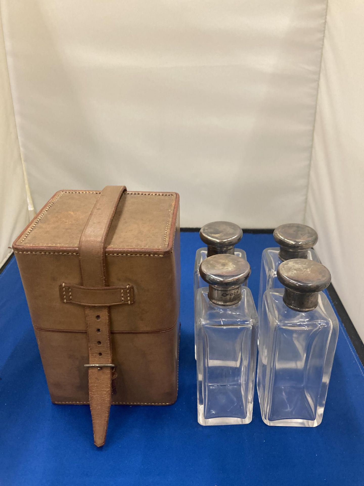 A VINTAGE LEATHER CASE CONTAINING FOUR GLASS BOTTLES WITH HALLMARKED SILVER TOPS
