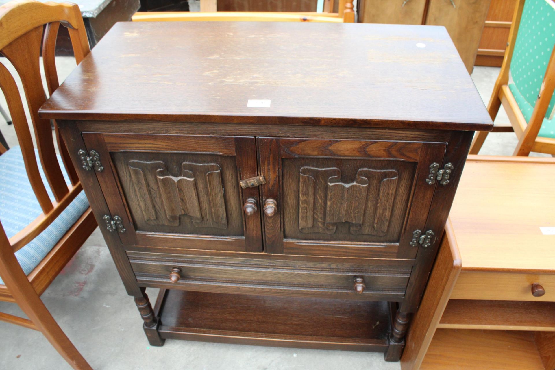 AN OAK JACOBEAN STYLE TWO DOOR LINEN FOLD CUPBOARD WITH SINGLE DRAWER ON AN OPEN BASE WITH TURNED