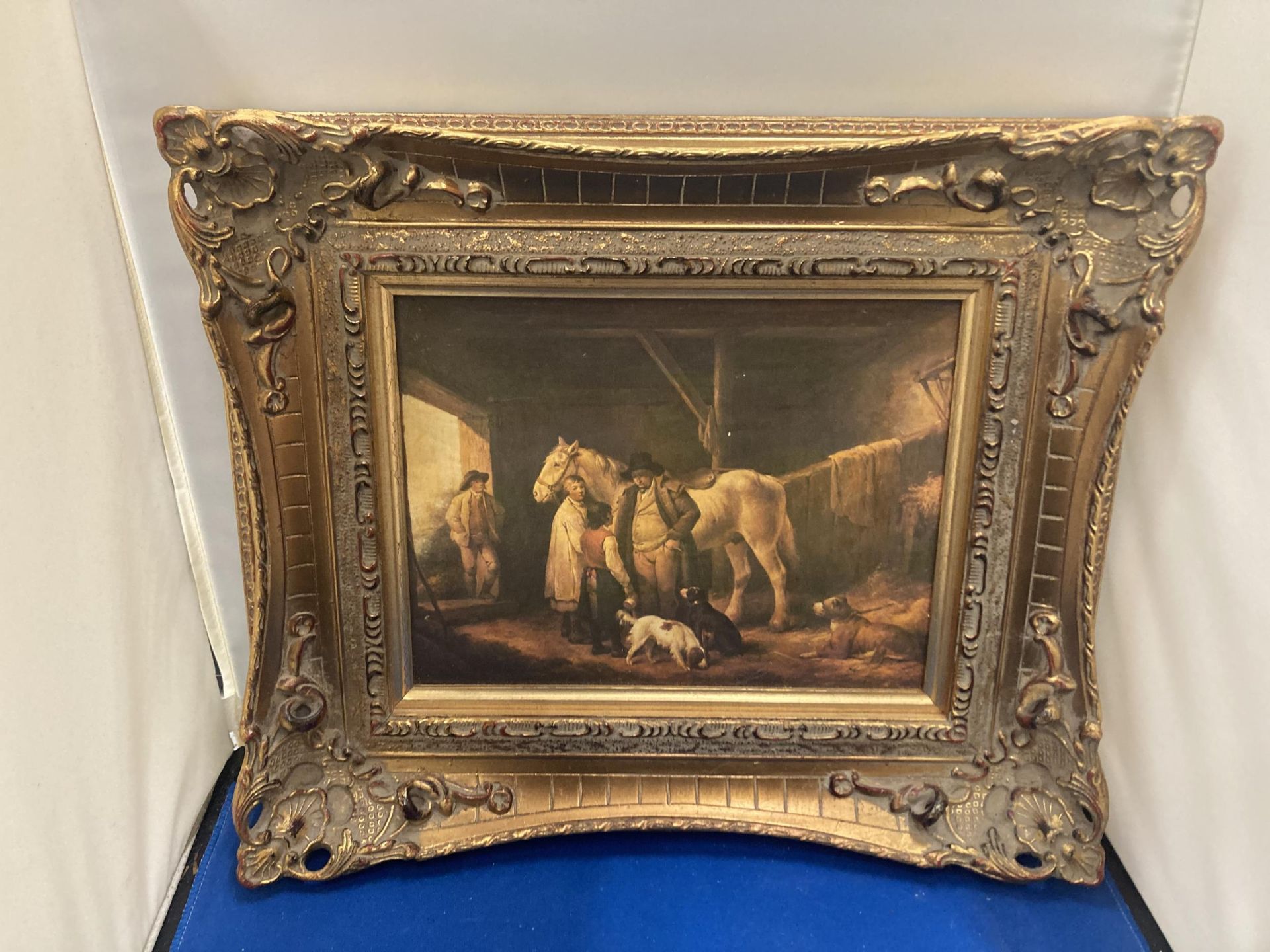 A GILT FRAMED PRINT OF A FAMILY AND DOGS IN A STABLE WITH A HORSE 17CM X 22CM