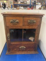 A VINTAGE OAK SMOKERS CABINET WITH TWO SHORT UPPER DRAWERS, A GLAZED DOOR AND A LONG LOWER DRAWER