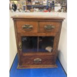 A VINTAGE OAK SMOKERS CABINET WITH TWO SHORT UPPER DRAWERS, A GLAZED DOOR AND A LONG LOWER DRAWER