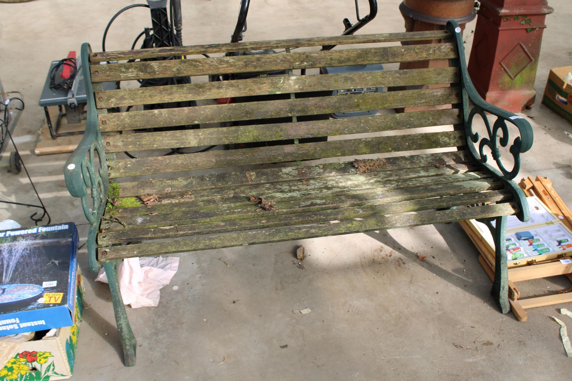 A WOODEN SLATTED GARDEN BENCH WITH DECORATIVE CAST BENCH ENDS