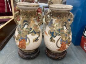 A PAIR OF TWIN HANDLED SATSUMA VASES ON WOODEN STANDS