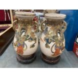 A PAIR OF TWIN HANDLED SATSUMA VASES ON WOODEN STANDS