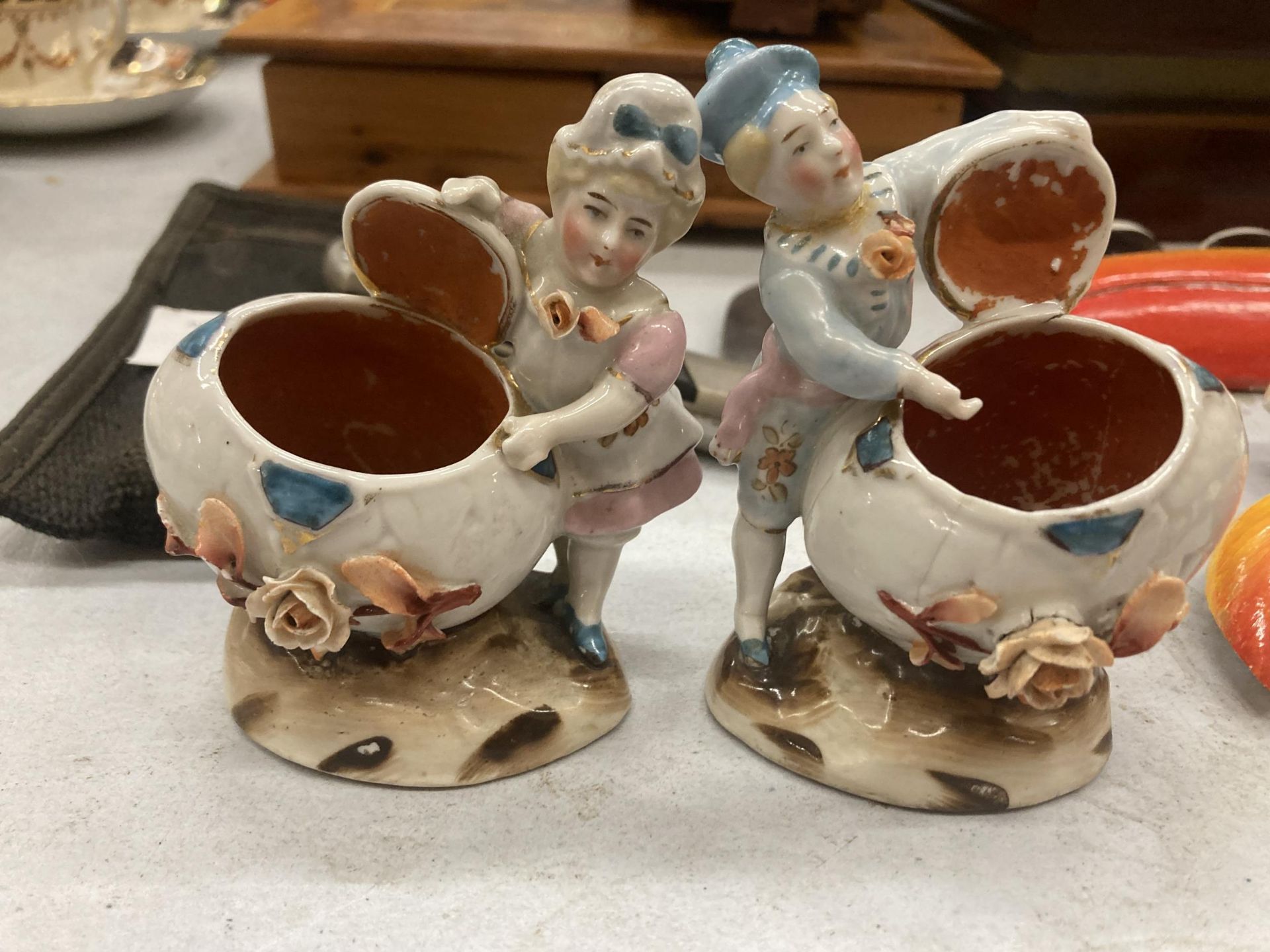 TWO VINTAGE GERMAN MATCHSTICK HOLDER FAIRINGS DEPICTING A LADY AND A MAN WITH AN OPEN FLOWERED SHELL