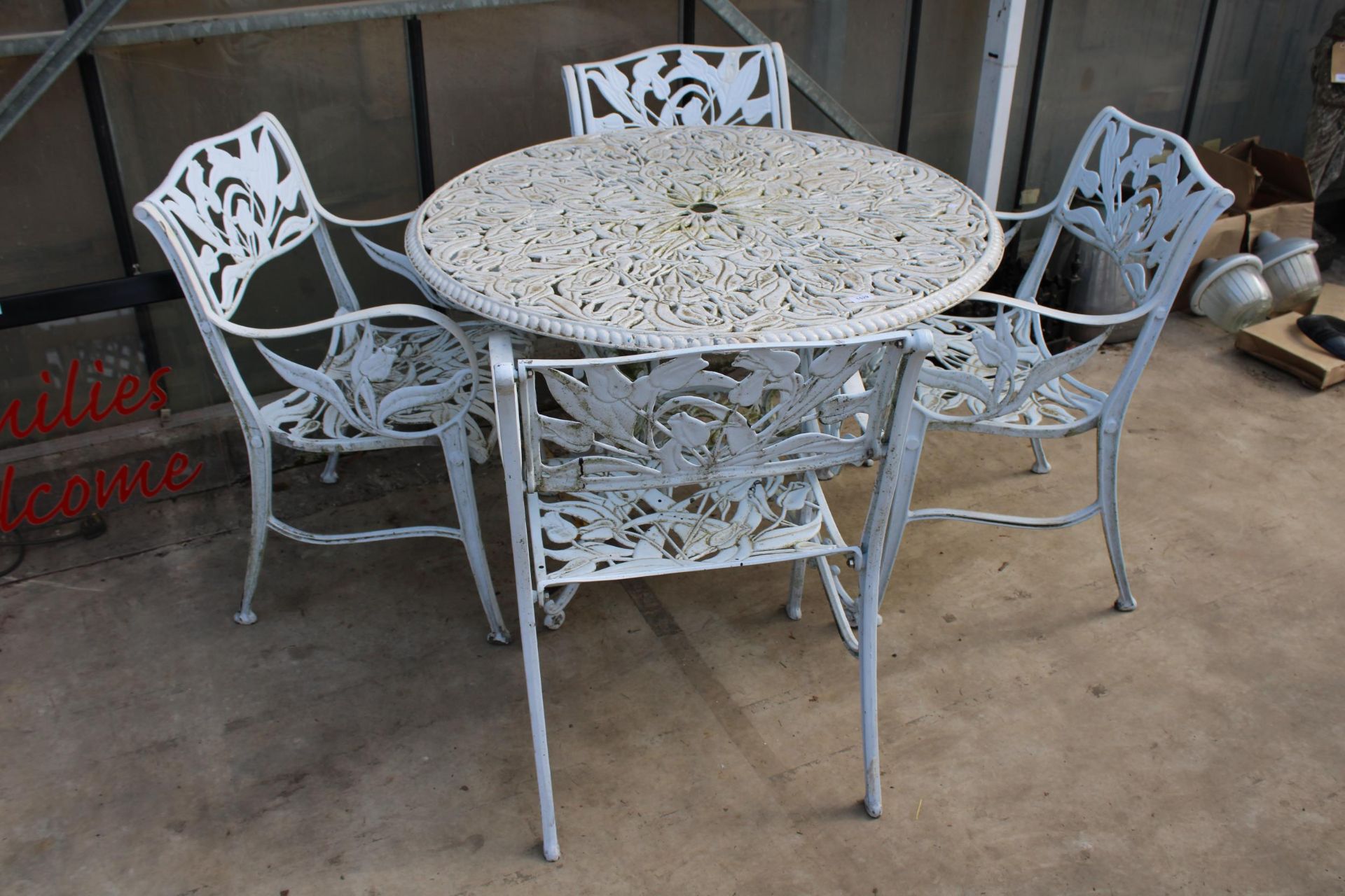 A WHITE CAST ALLOY BISTRO SET COMPRISING OF A LARGE ROUND TABLE AND FOUR CARVER CHAIRS