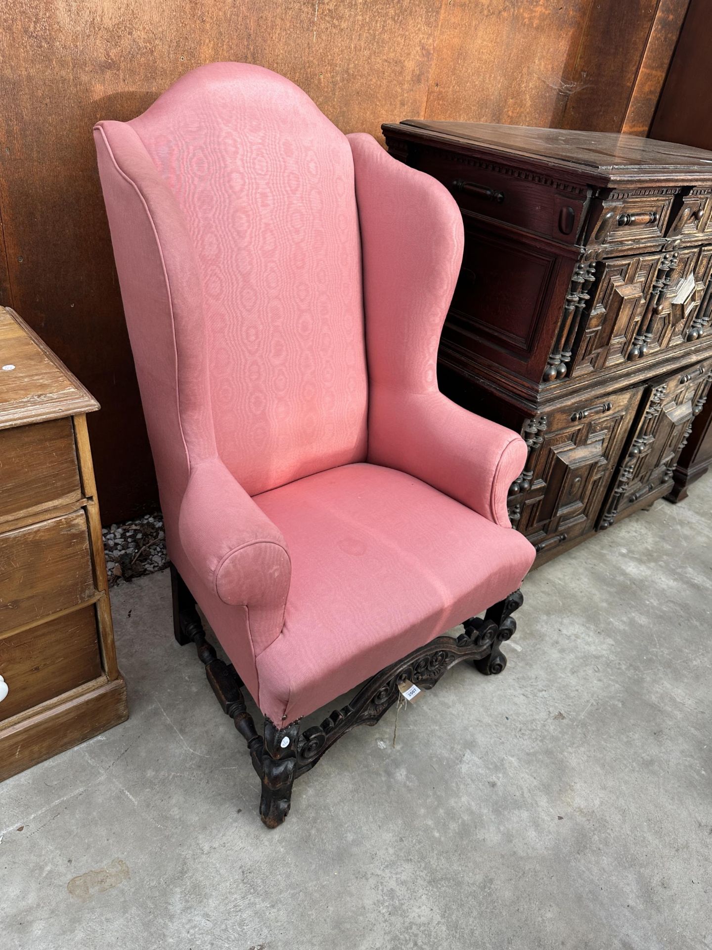 AN OAK FRAMED JACOBEAN STYLE WINGED LOUNGE CHAIR WITH CARVED FRONT PANEL LOOP WITH TURNED STRETCHERS