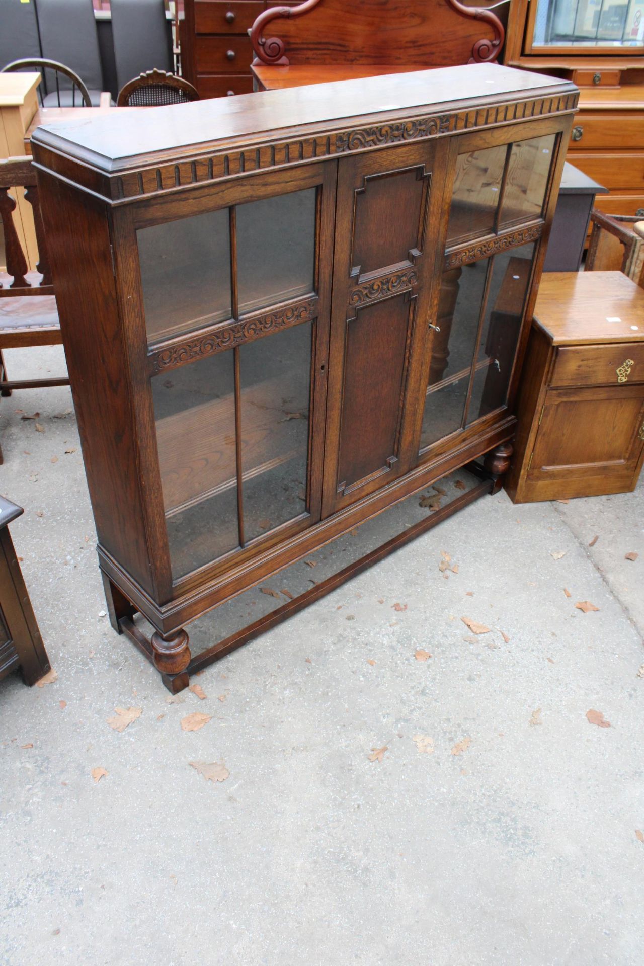 AN EARLY 20TH CENTURY OAK TWO DOOR DISPLAY CABINET ON OPEN BASE WITH TURNED FRONT LEGS, 48" WIDE