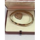 TWO 9 CARAT GOLD PLATED ITEMS - A BANGLE AND A HEART SHAPED LOCKET