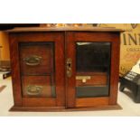 AN OAK TWO GLASS DOOR SMOKERS CABINET WITH THREE INTERIOR DRAWERS ONE LABELED PLAYING CARDS COMPLETE