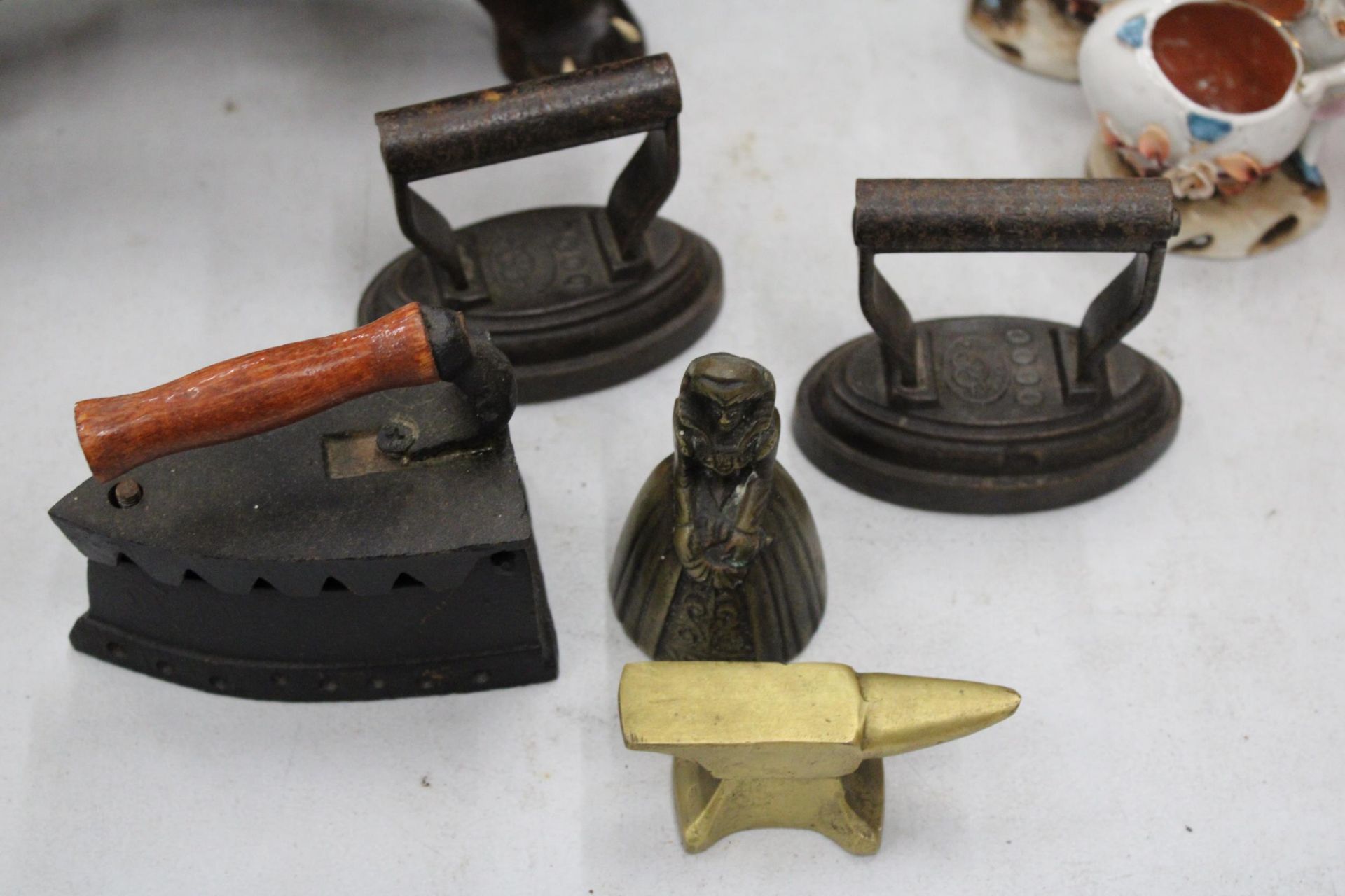 A COLLECTION OF MINIATURE ITEMS TO INCLUDE THREE IRONS, A BRASS ANVIL AND A 'LADY' BELL