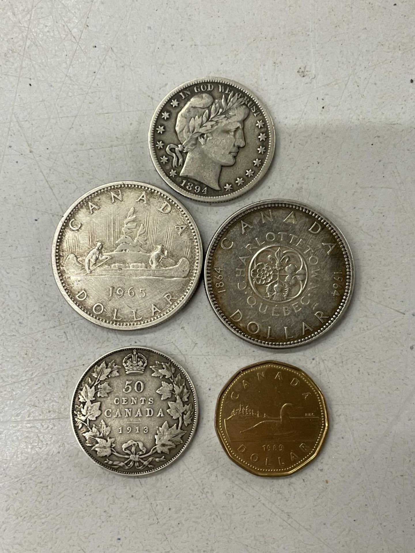 AN 1894 US HALF DOLLAR AND FOUR CANADIAN COINS TO INCLUDE A 1964 AND A 1965 DOLLAR, A 1913 50 CENT