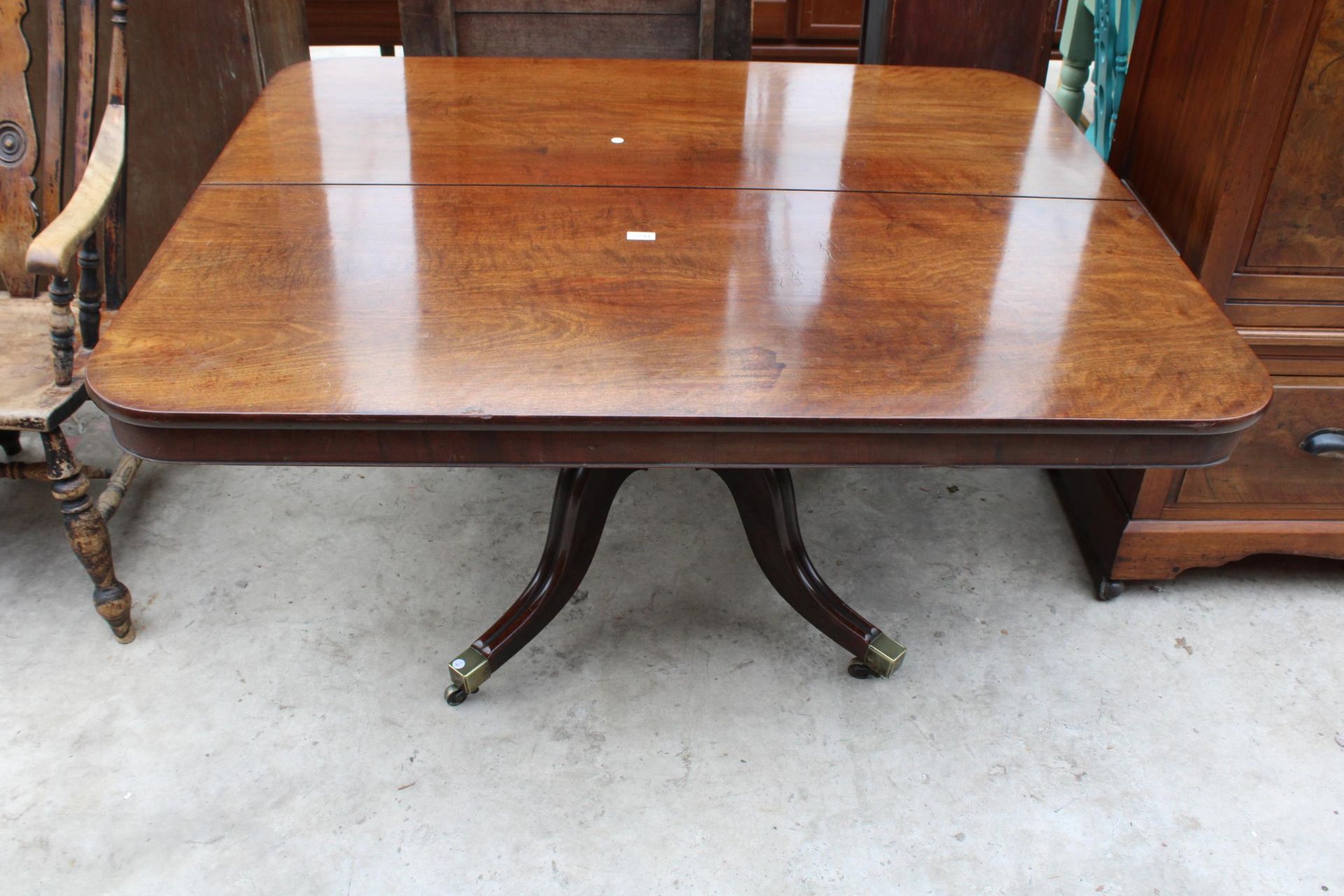 A REGENCY STYLE MAHOGANY PEDESTAL TILT-TOP DINING TABLE 56" X 46.5" WITH BRASS FEET AND CASTERS