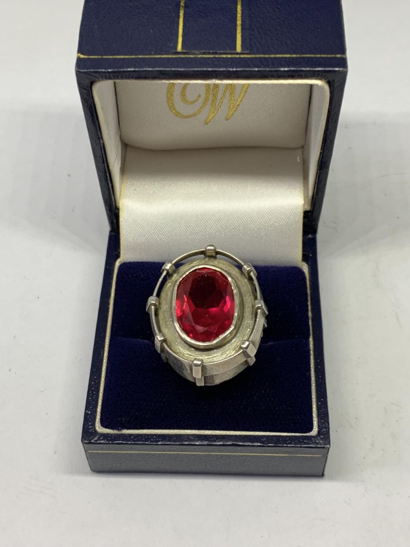 AN OVAL DESIGNER RING WITH RED STONE IN A PRESENTATION BOX