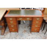 AN EDWARDIAN MAHOGANY KNEE HOLE DESK ENCLOSING SEVEN DRAWERS WITH BRASS HANDLES AND INSET LEATHER