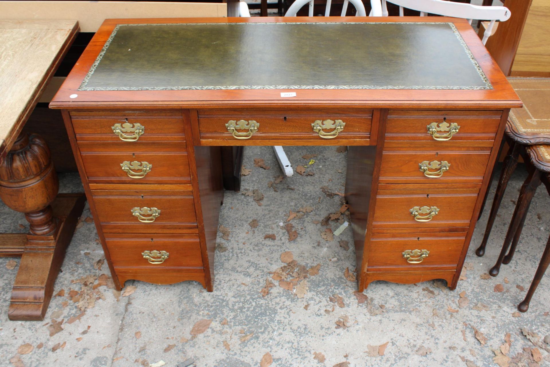 AN EDWARDIAN MAHOGANY KNEE HOLE DESK ENCLOSING SEVEN DRAWERS WITH BRASS HANDLES AND INSET LEATHER