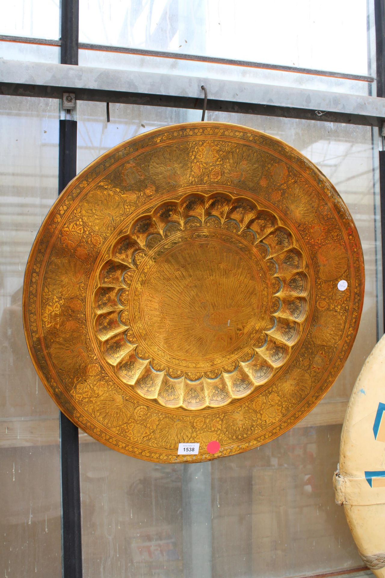 A LARGE BRASS WALL CHARGER DEPICTING A PEACOCK