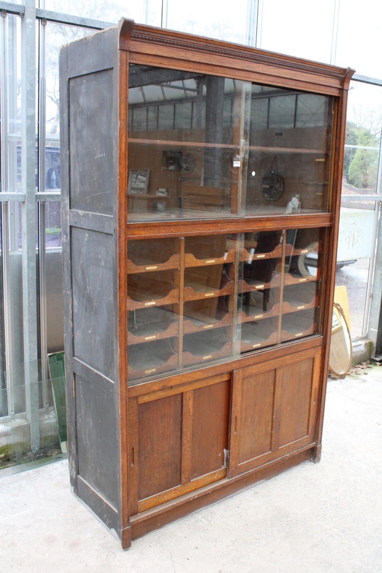 AN EARLY 20TH CENTURY OAK HABERDASHERY CABINET ENCLOSING 16 SLIDES, 4 SLIDING DOORS, 2 BEING GLASS