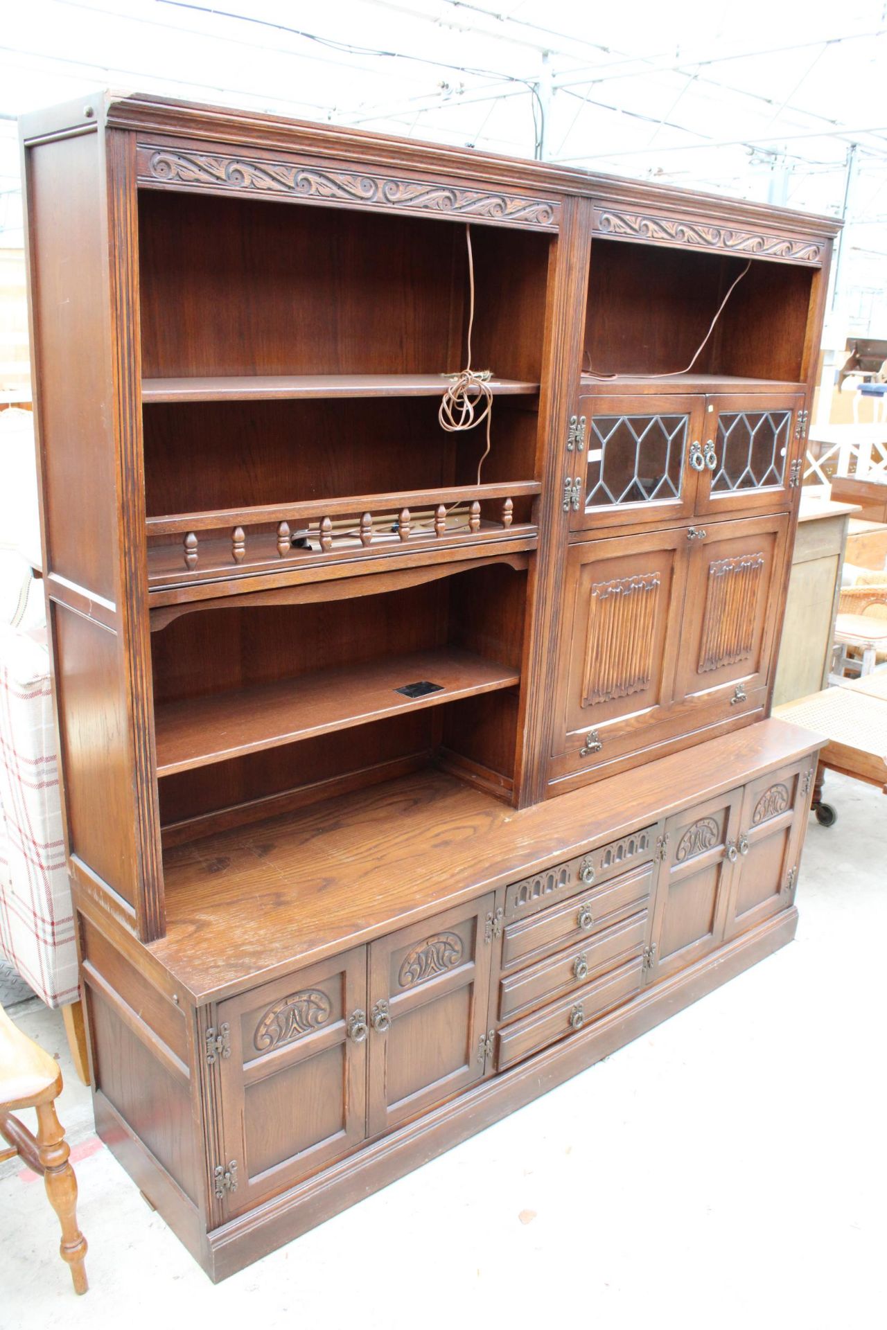 AN OAK OLD CHARM LOUNGE UNIT WITH GLAZED AND LEADED LINEN FOLD DOORS WITH CUPBOARDS AND DRAWERS TO