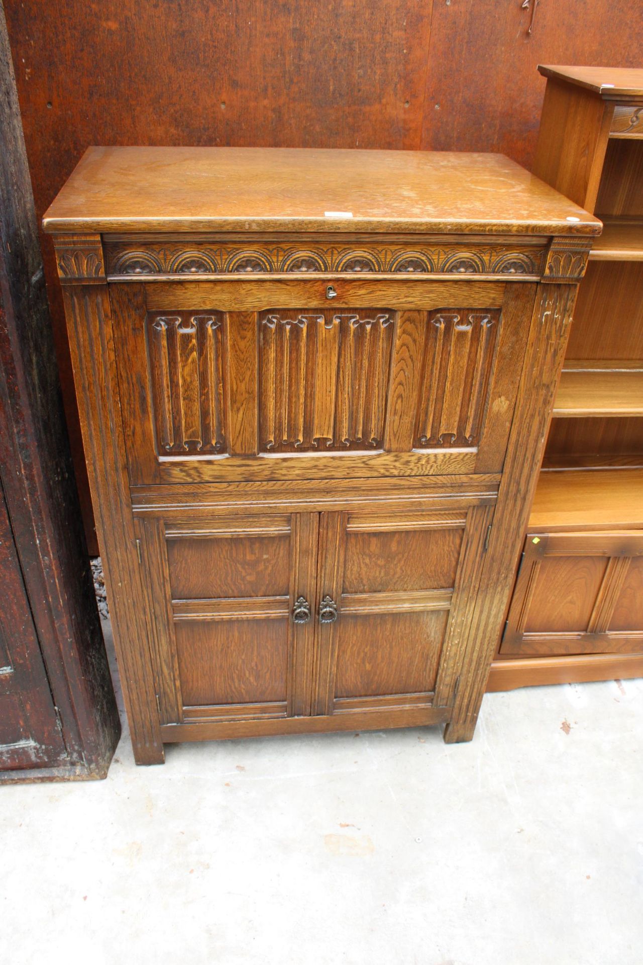 AN OAK CHARM STYLE COCKTAIL CABINET WITH LINEN-FOLD DROP DOWN FRONT AND CUPBOARD TO BASE, 31.5" WIDE