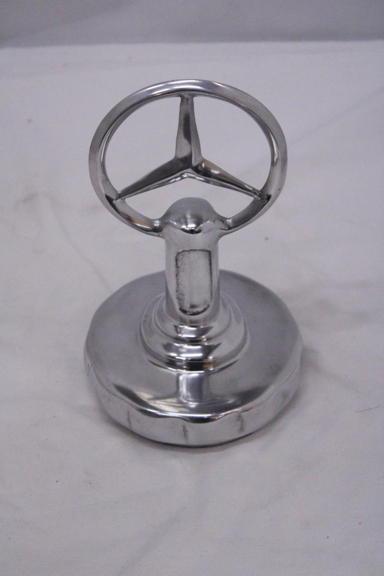 A CHROME MERCEDES BENZ EMBLEM ON A BASE, HEIGHT 23CM