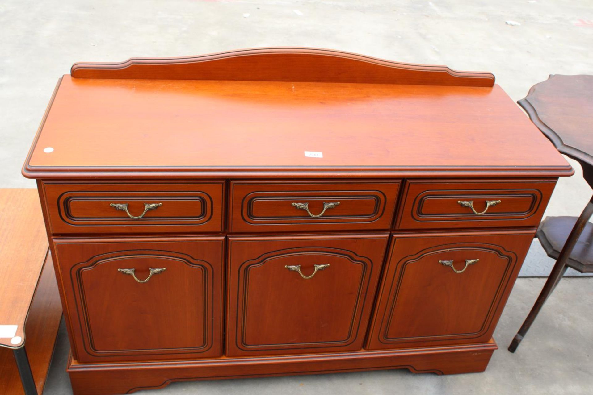 A MODERN CHERRY WOOD EFFECT SIDEBOARD ENCLOSING THREE DRAWERS AND THREE CUPBOARDS WITH RAISED