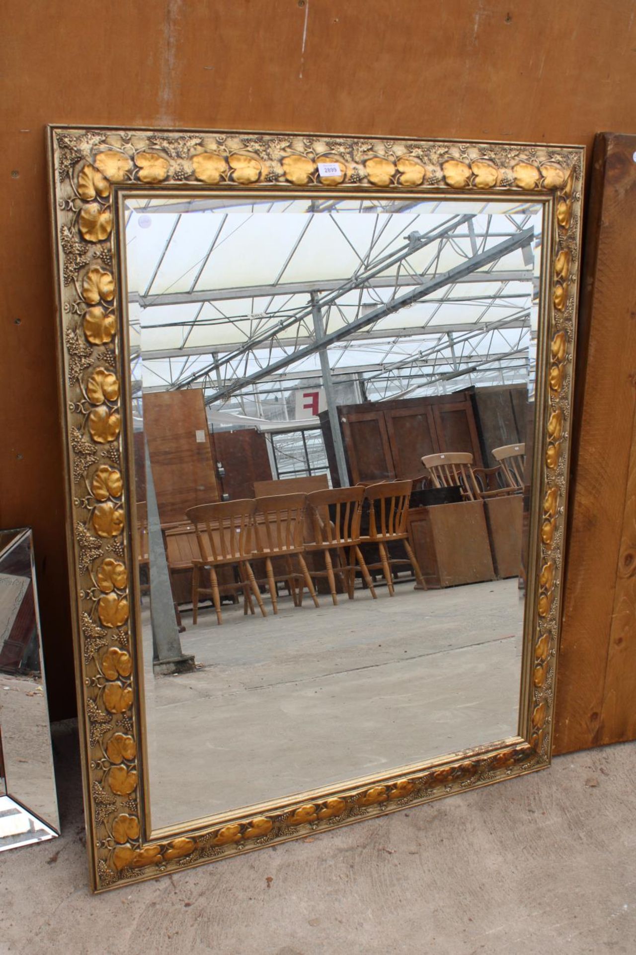 A MODERN GILT FRAMED WALL MIRROR WITH BEVEL EDGE AND FOLIATE DECORATION, 48" X 37"