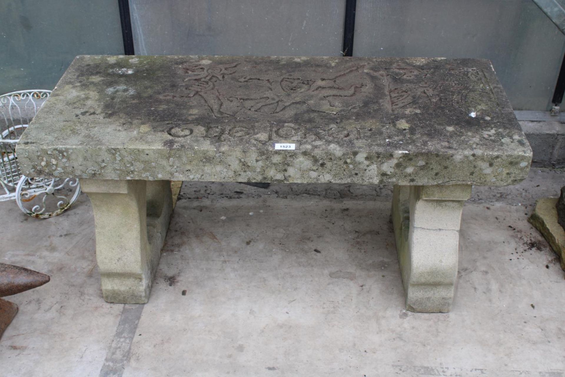 A NATURAL STONE HAND CARVED BENCH WITH 'THE JOKER' DETAIL AND PEDESTAL BASES (REQUIRES FIXING ONTO