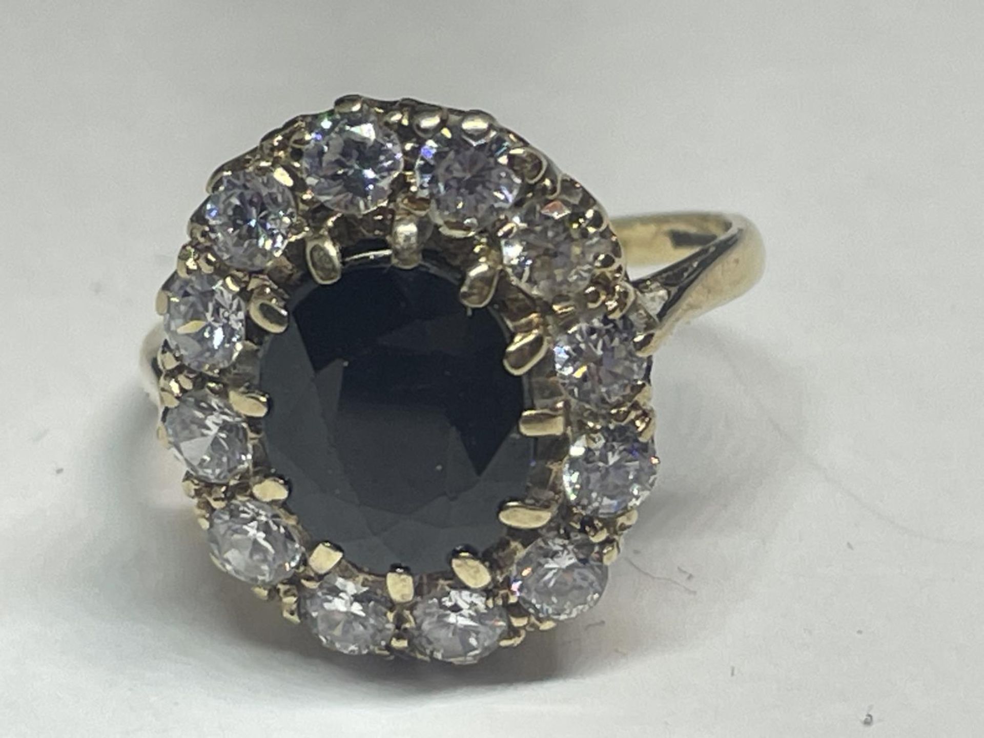 A 9 CARAT GOLD DRESS RING WITH CENTRE BLUE STONE SURROUNDED BY CUBIC ZIRCONIAS SIZE Q IN A - Image 2 of 5