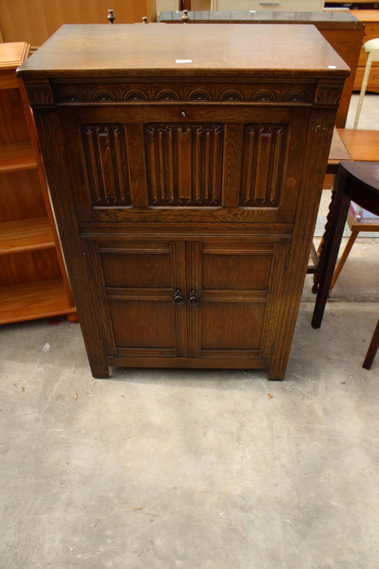 AN OAK CHARM STYLE COCKTAIL CABINET WITH LINEN-FOLD DROP DOWN FRONT AND CUPBOARD TO BASE, 31.5" WIDE