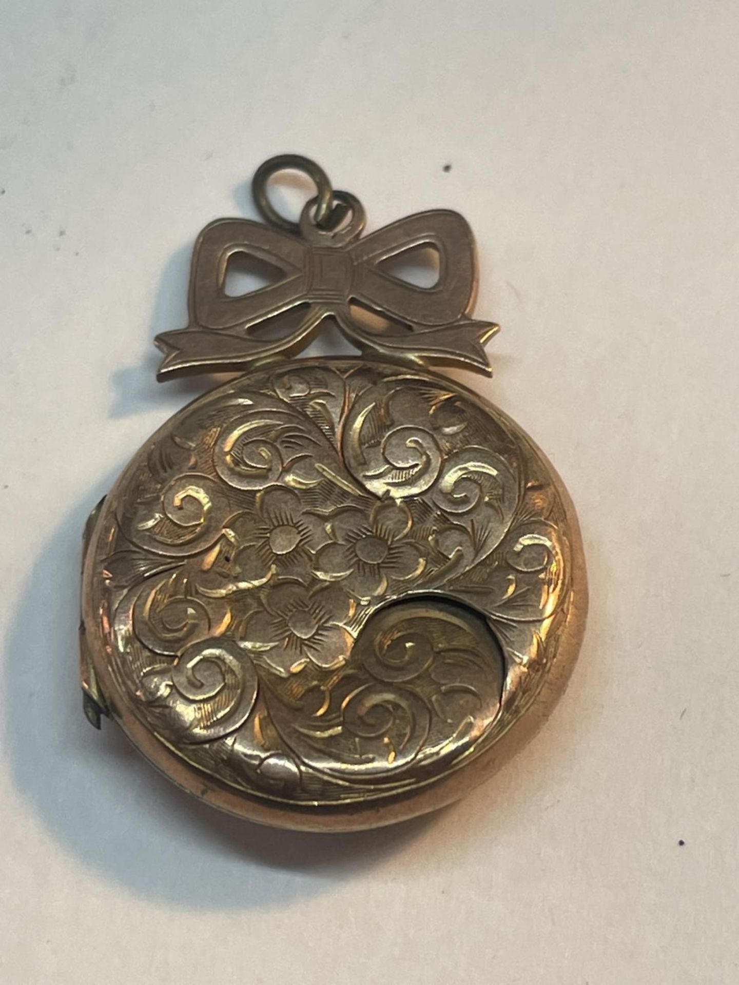 A 9 CARAT GOLD (INDISTINCT HALLMARK) LOCKET WITH BOW DESIGN TO INCLUDE VINTAGE PHOTOGRAPHS GROSS