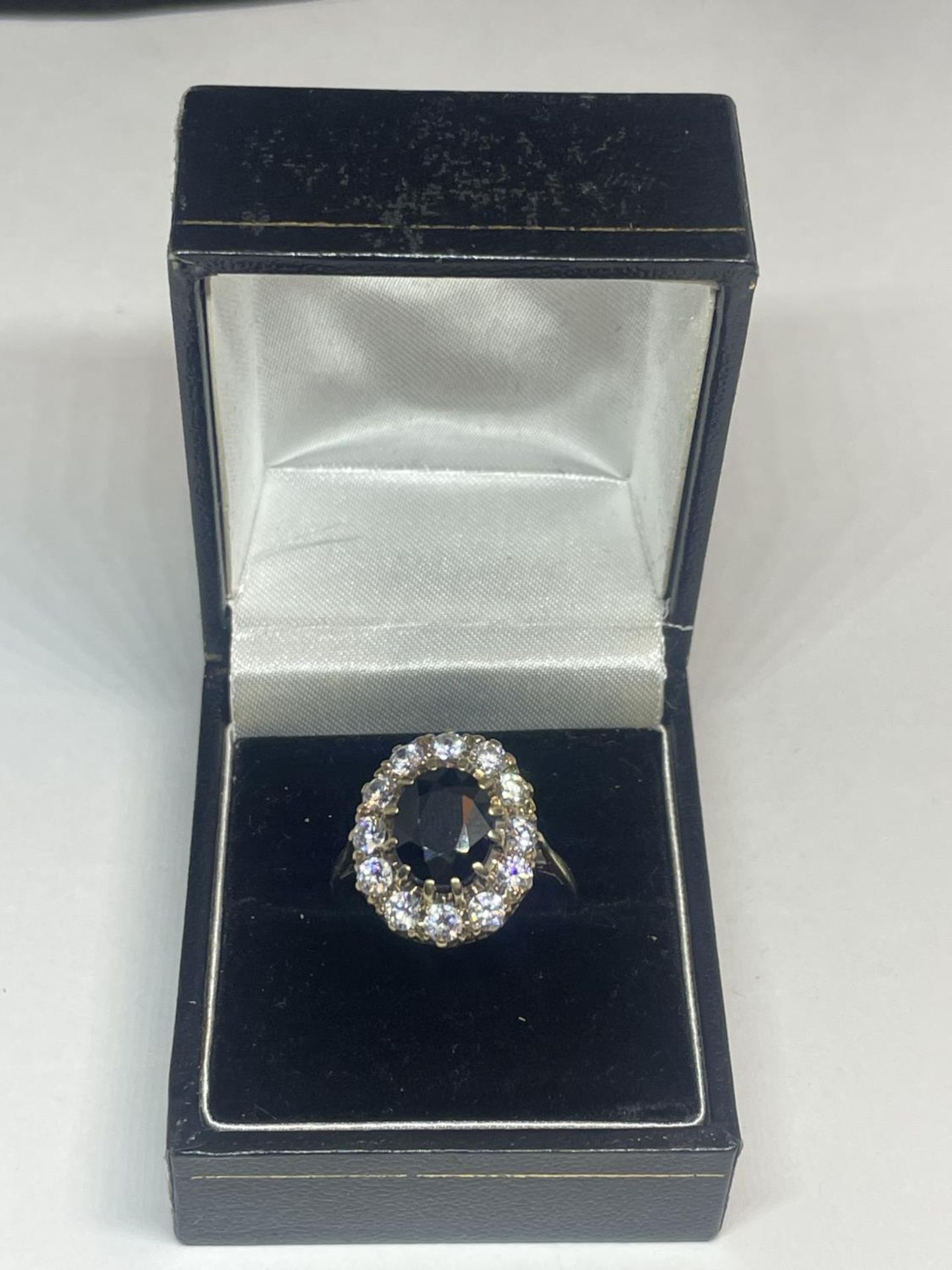 A 9 CARAT GOLD DRESS RING WITH CENTRE BLUE STONE SURROUNDED BY CUBIC ZIRCONIAS SIZE Q IN A