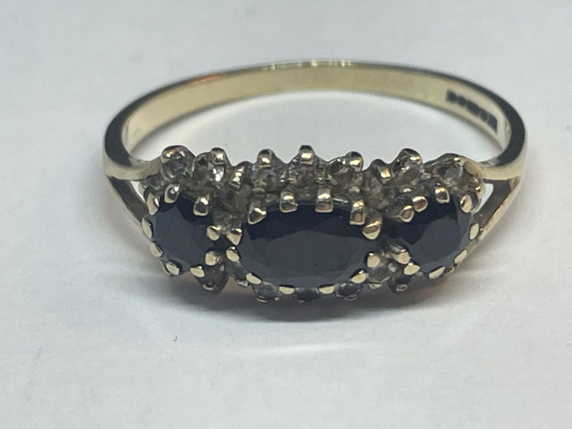 A 9 CARAT GOLD RING WITH THREE IN LINE SAPPHIRES SURROUNDED BY CUBIC ZIRCONIAS SIZE Q