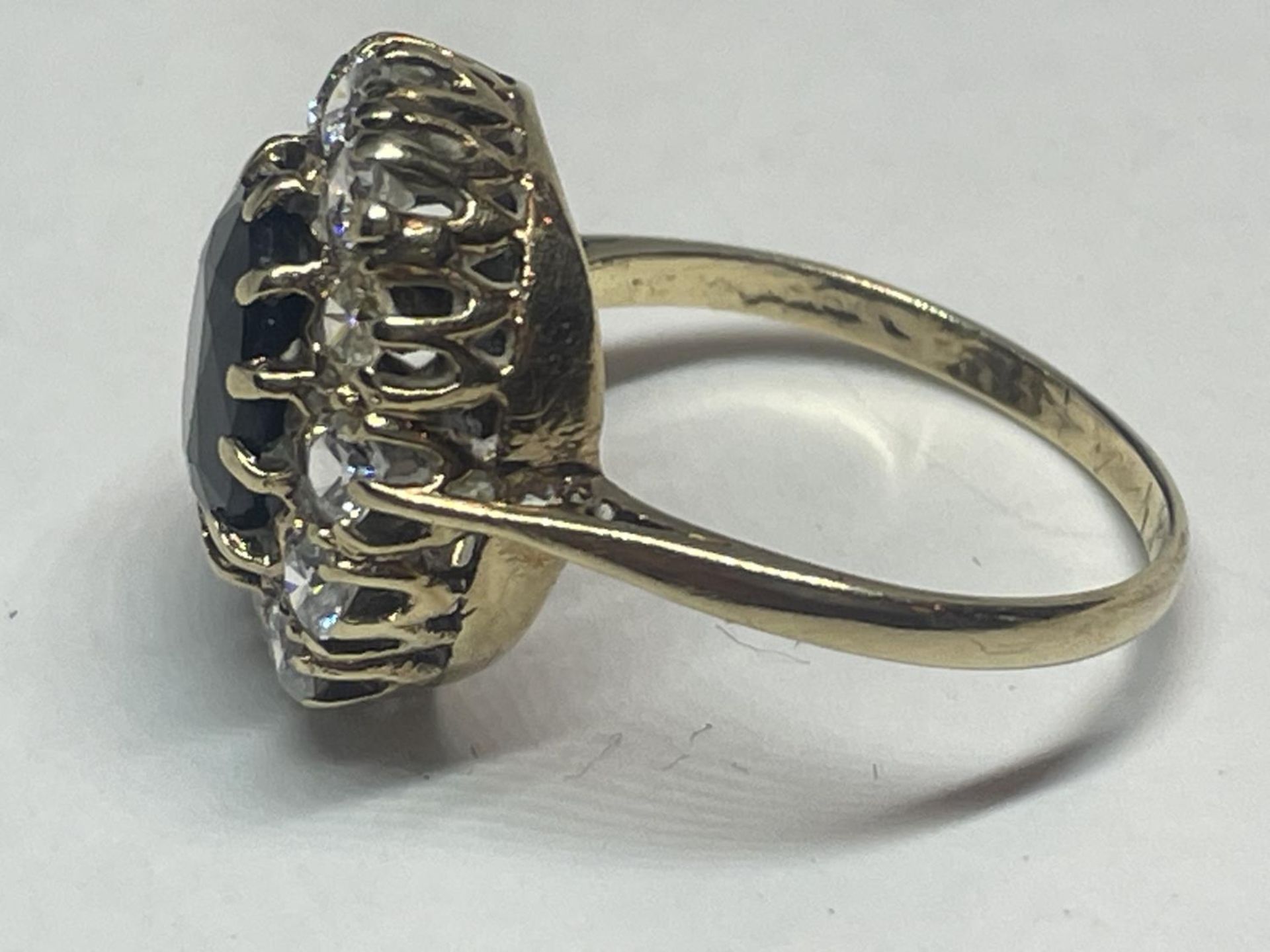 A 9 CARAT GOLD DRESS RING WITH CENTRE BLUE STONE SURROUNDED BY CUBIC ZIRCONIAS SIZE Q IN A - Image 3 of 5
