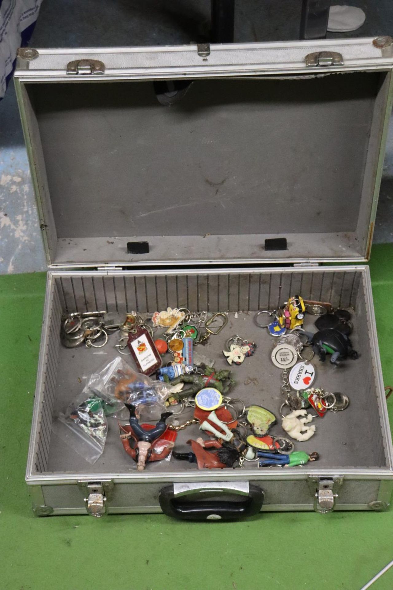 A METAL STORAGE CASE CONTAINING A SELECTION OF VINTAGE KEYRINGS AND FIGURES