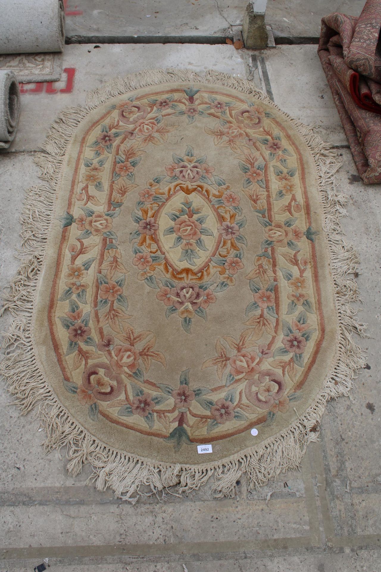AN OVAL PEACH PATTERNED FRINGED RUG