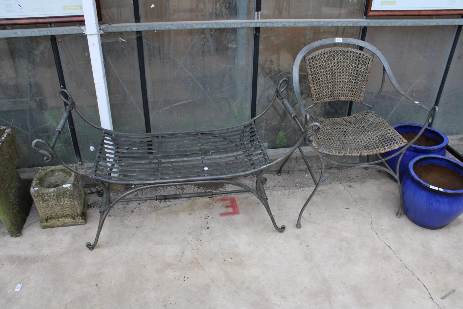 A METAL GARDEN CHAIR WITH RATTAN SEAT AND BACK AND A SIMILAR HEAVY METAL BENCH