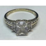 A 9 CARAT GOLD RING WITH A LARGE CENTRE CUBIC ZIRCONIA AND SMALLER TO THE SHOULDERS SIZE O