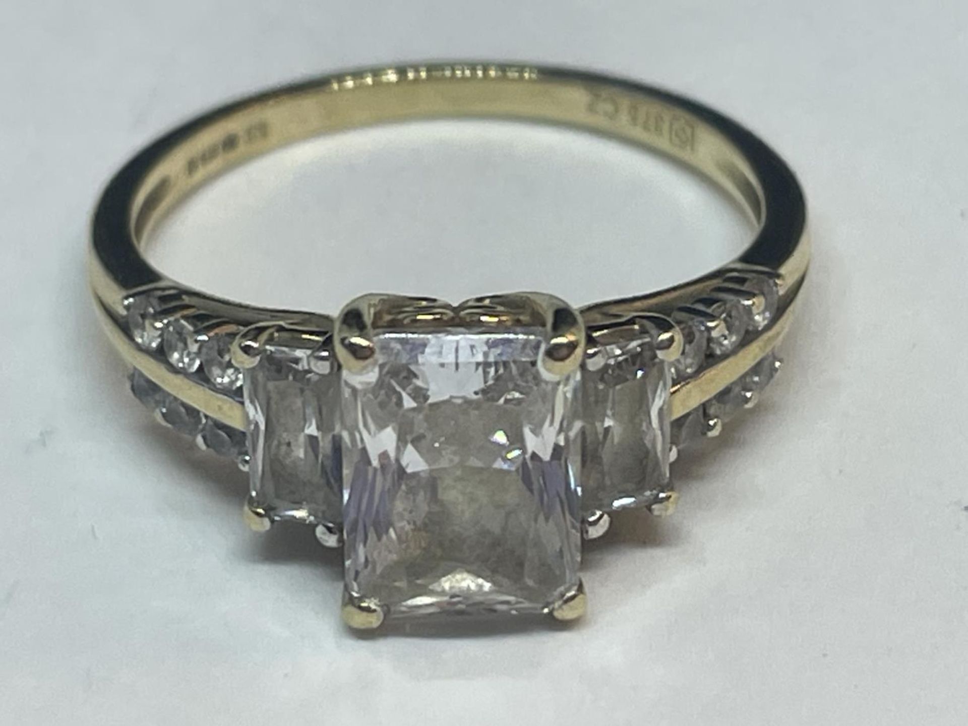 A 9 CARAT GOLD RING WITH A LARGE CENTRE CUBIC ZIRCONIA AND SMALLER TO THE SHOULDERS SIZE O