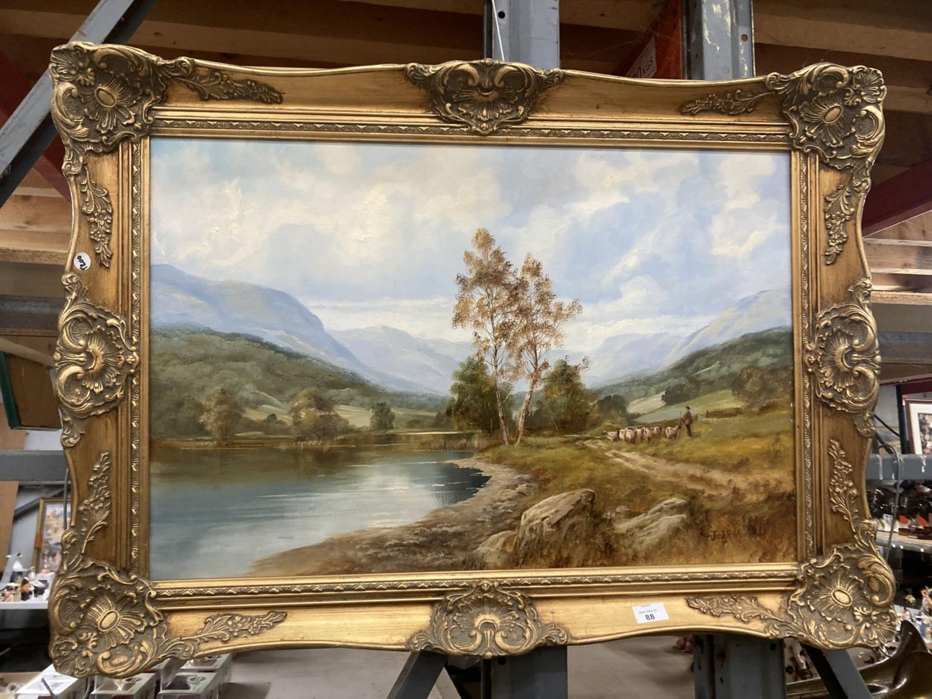 A GILT FRAMED OIL ON CANVAS OF A LAKE SCENE WITH A FARMER MOVING STOCK SIGNED JACK R MOULD TO