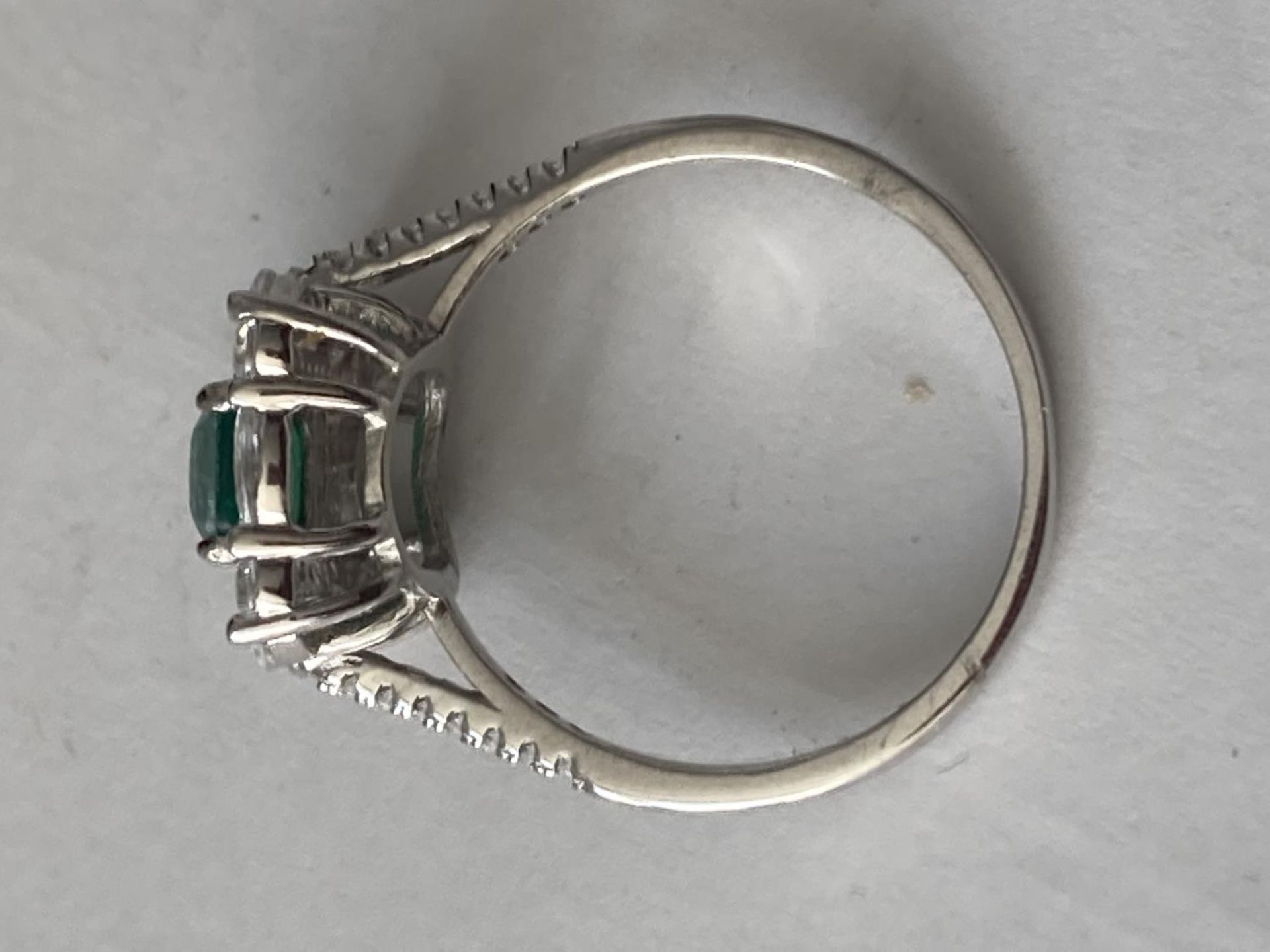 A WHITE METAL RING WITH A CENTRE RECTANGULAR LABORATORY GROWN EMERALD SURROUNDED BY CLEAR STONES - Image 5 of 6