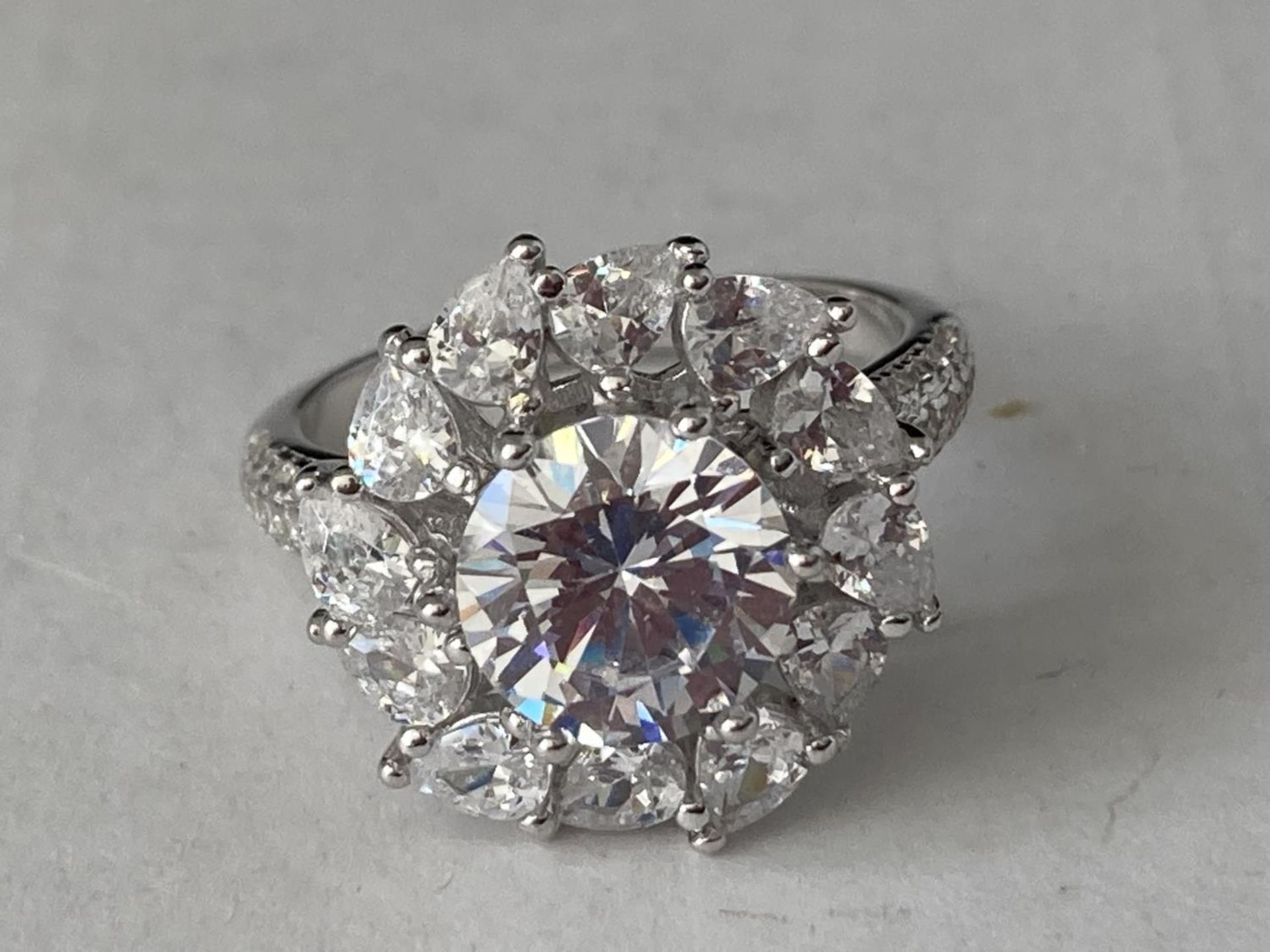 A WHITE METAL RING WITH 3 CARATS OF MOISSANITE IN A FLOWER DESIGN AND ON THE SHOULDERS SIZE P/Q