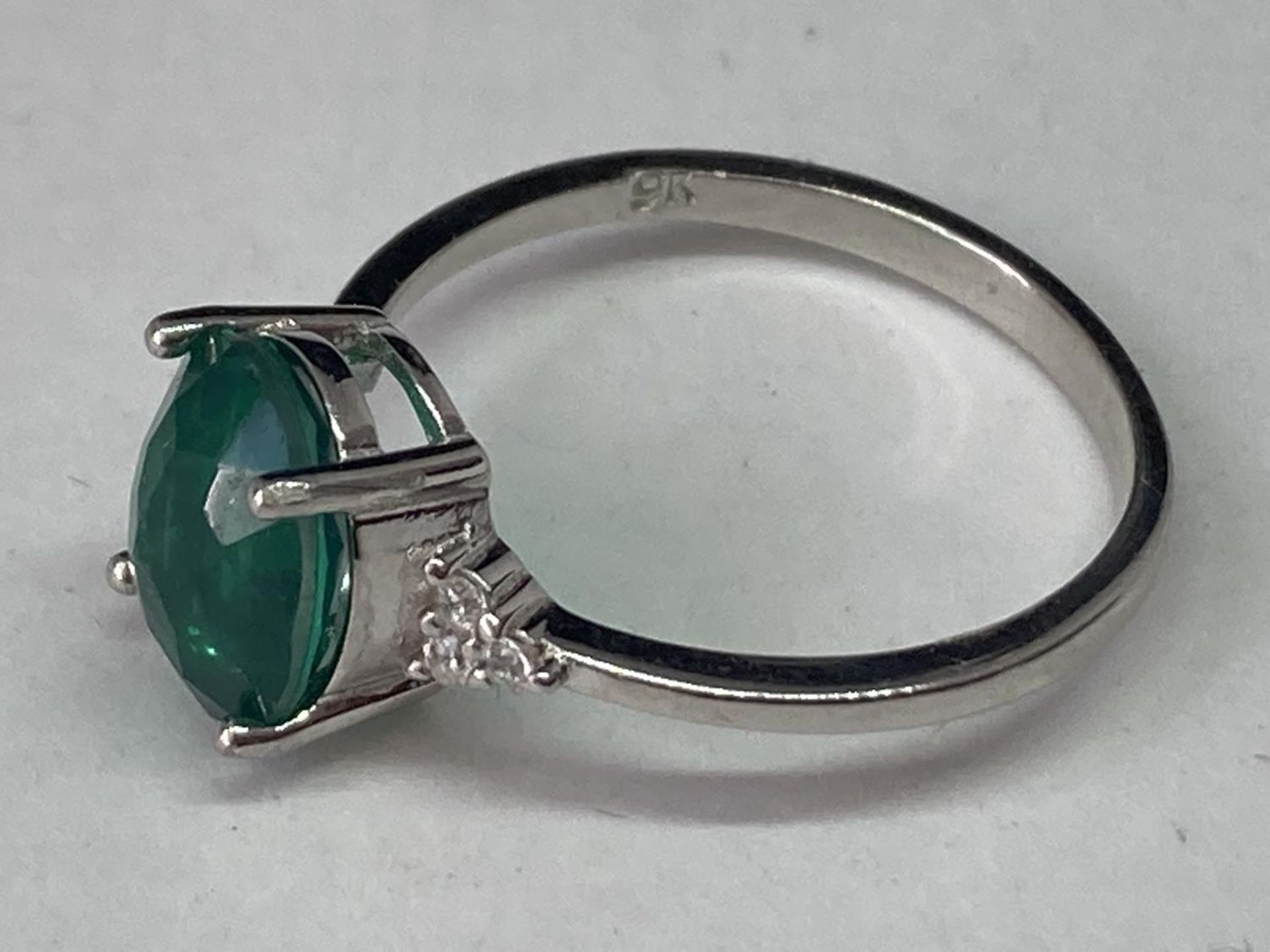 A WHITE METAL RING WITH AN OVAL LABORATORY EMERALD WITH THREE CLEAR STONES TO EACH SIDE SIZE Q/R - Image 3 of 6