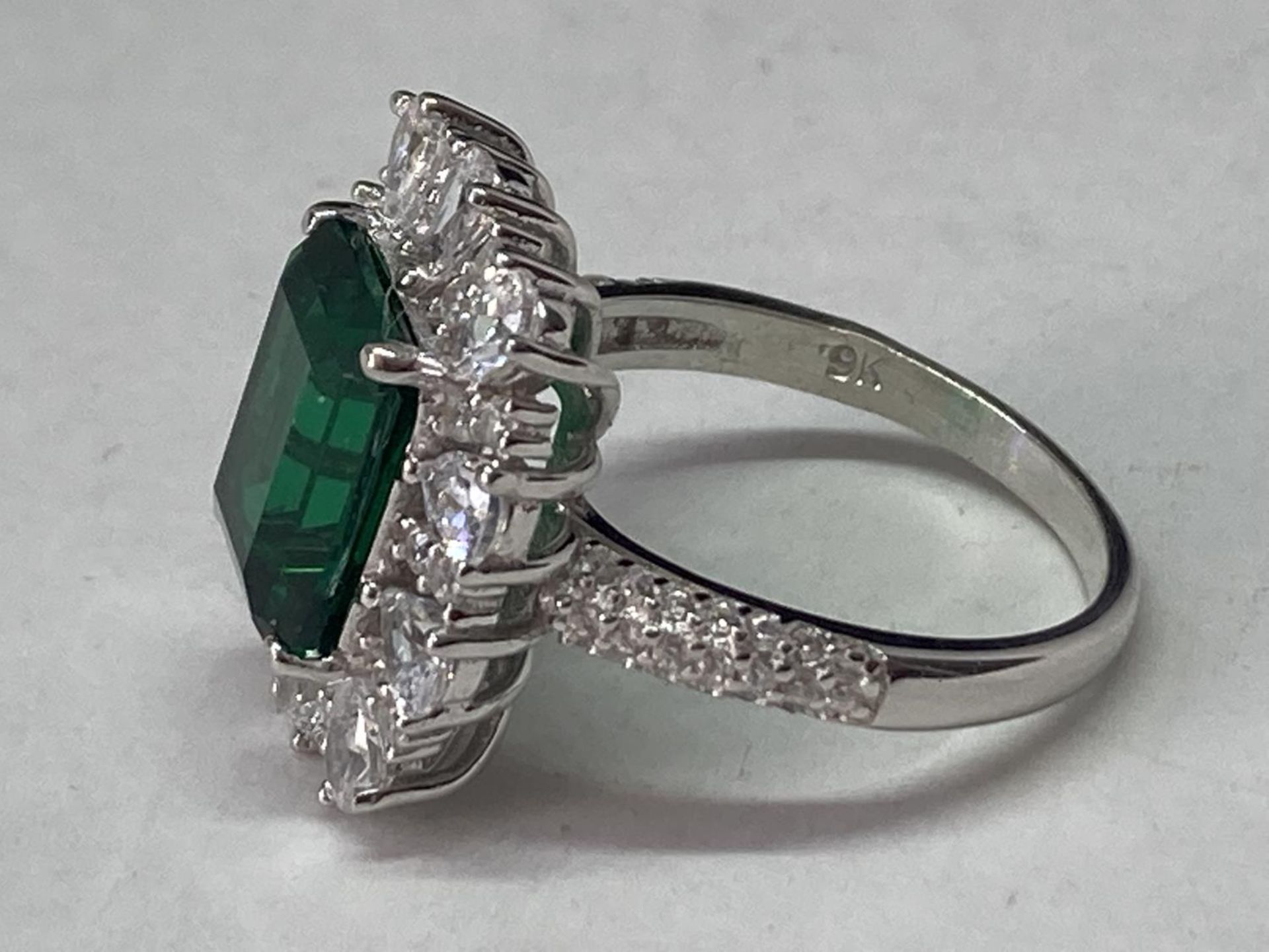 A WHITE METAL RING WITH A LARGE RCTANGULAR LABORATORY EMERALD SURROUNDED BY CLEAR STONES ALSO ON THE - Image 4 of 8
