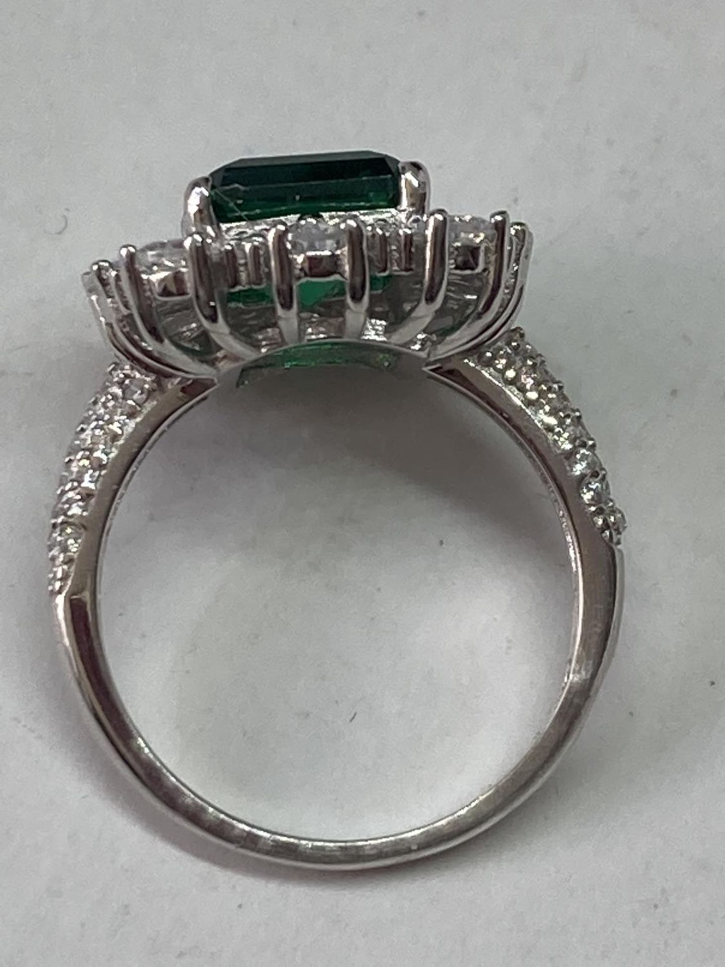 A WHITE METAL RING WITH A LARGE RCTANGULAR LABORATORY EMERALD SURROUNDED BY CLEAR STONES ALSO ON THE - Image 7 of 8