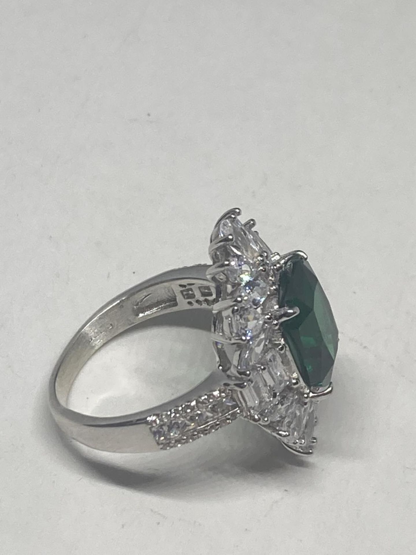 A WHITE METAL RING WITH A LARGE CENTRE LABORATORY GROWN EMERALD SURROUNDED BY CLEAR STONES SIZE S - Image 7 of 8