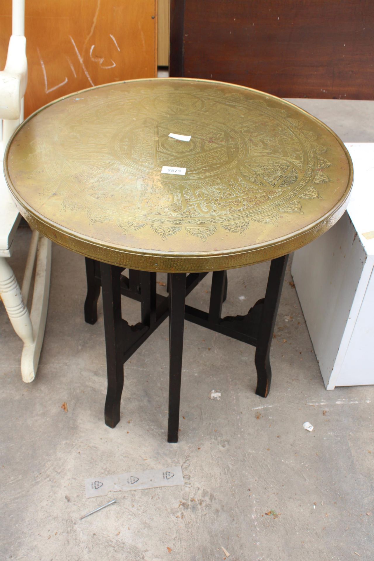 A BRASS 23" DIAMETER INDIAN COFFEE TABLE ON EBONISED FOLDING BASE