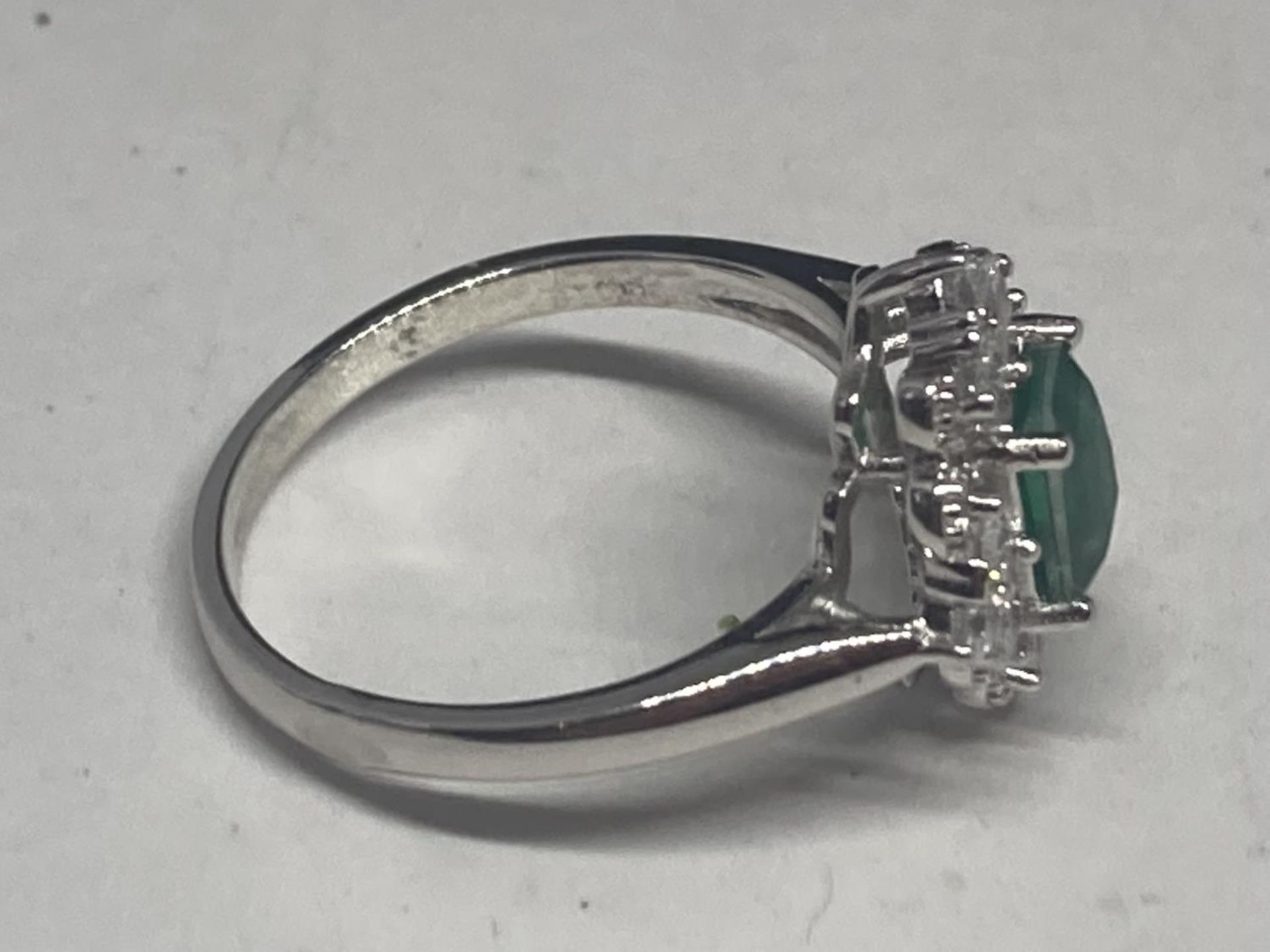 A WHITE METAL RING WITH A RECTANGULAR LABORATORY EMERALD SURROUNDED BY CLEAR STONES SIZE Q/R - Image 8 of 8